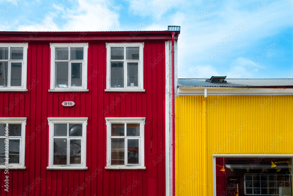 Reykjavik, Iceland - Apr 28 2019: Typical fisherman's colorful houses in Reykjavik with red and yellow metallic facade and white six framed wooden windows. Colorful contrast concept. Blue cloudy sky.