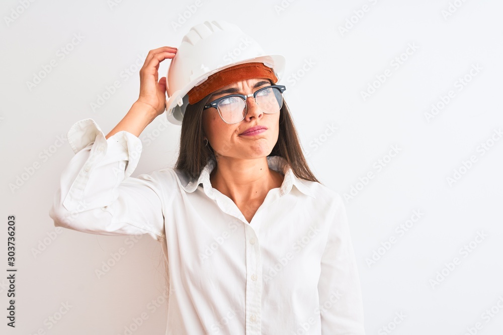 Young beautiful architect woman wearing helmet and glasses over isolated white background confuse and wonder about question. Uncertain with doubt, thinking with hand on head. Pensive concept. Young beautiful architect woman wearing helmet and glasses over isolated white background confuse and wonder about question. Uncertain with doubt, thinking with hand on head. Pensive concept.