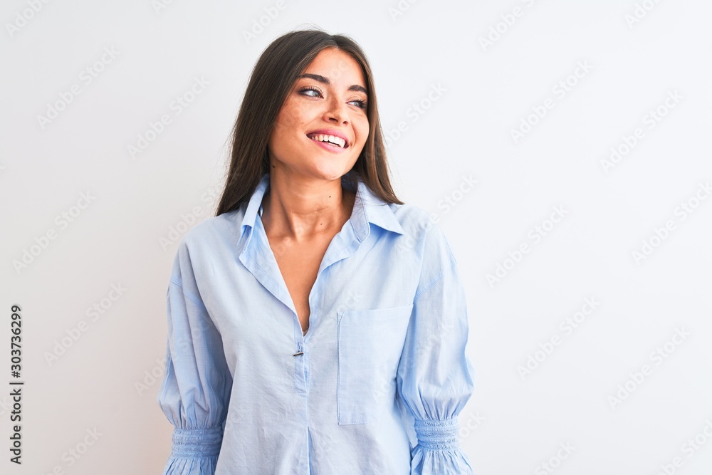 Young beautiful woman wearing blue elegant shirt standing over isolated white background looking away to side with smile on face, natural expression. Laughing confident. Young beautiful woman wearing blue elegant shirt standing over isolated white background looking away to side with smile on face, natural expression. Laughing confident.