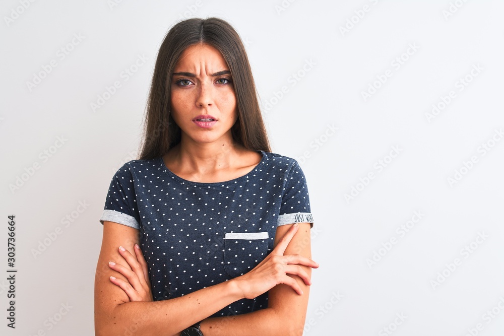 Young beautiful woman wearing blue casual t-shirt standing over isolated white background skeptic and nervous, disapproving expression on face with crossed arms. Negative person. Young beautiful woman wearing blue casual t-shirt standing over isolated white background skeptic and nervous, disapproving expression on face with crossed arms. Negative person.