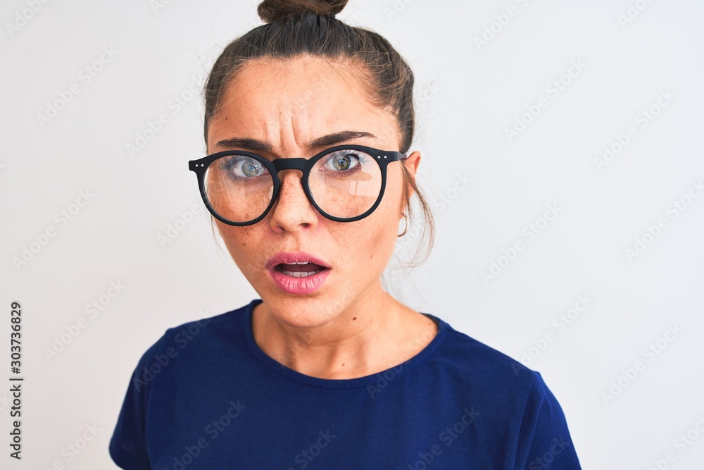 Beautiful woman with bun wearing blue t-shirt and glasses over isolated white background scared in shock with a surprise face, afraid and excited with fear expression Beautiful woman with bun wearing blue t-shirt and glasses over isolated white background scared in shock with a surprise face, afraid and excited with fear expression