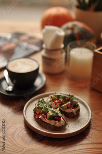 vegetarian food, sandwich with avocado, rucola and sun-dried tomatoes with a cup of coffee on the background, on a wooden table