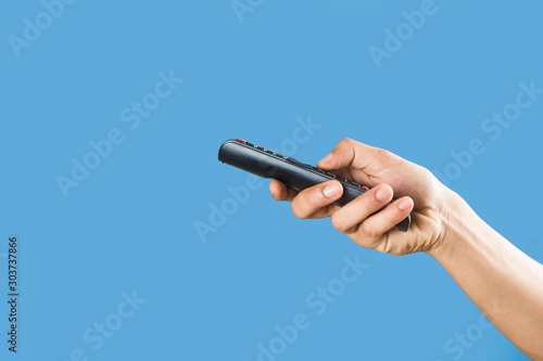 man's hand holding a TV remote control isolated on a light blue background 