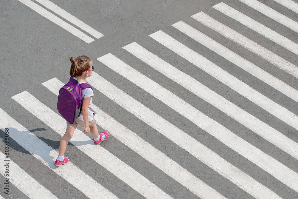 Schoolgirl crossing road on way to school. Zebra traffic walk way in the city. Concept pedestrians passing a crosswalk. Stylish young teen girl walking with backpack. Active child. Top view