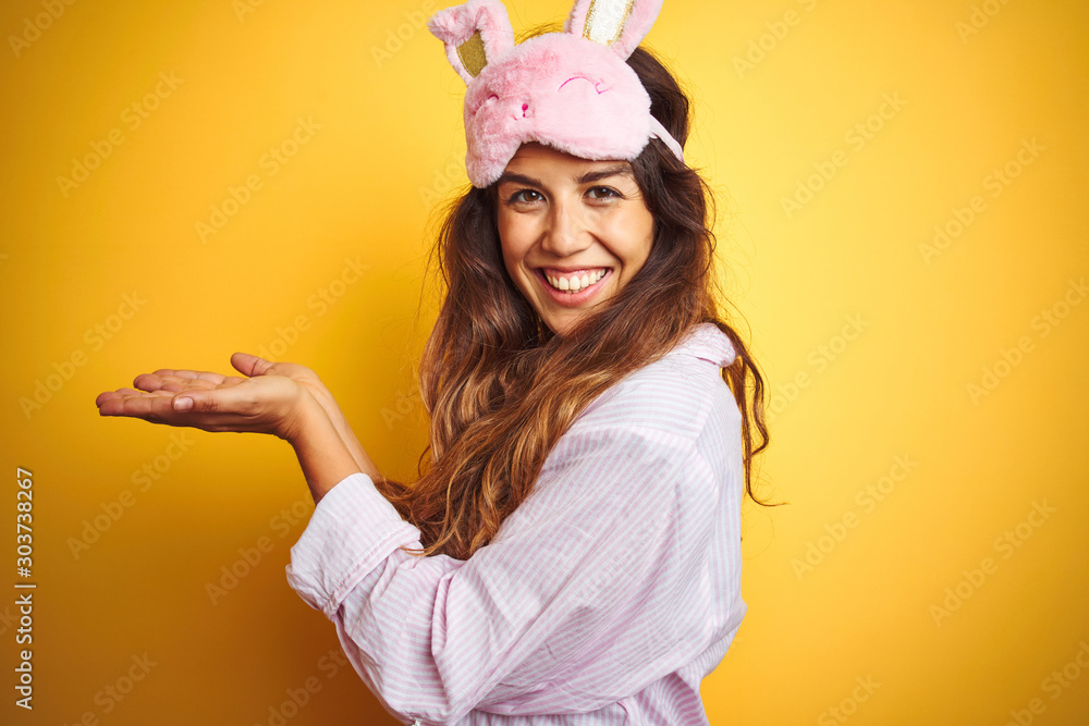 Φωτογραφία Young woman wearing pajama and sleep mask standing over yellow isolated backgrou