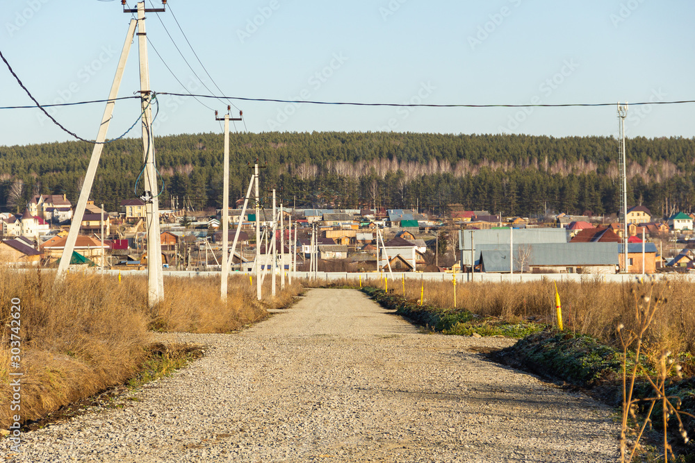 Dirt road with electric poles in a cottage village. Autumn, sunny