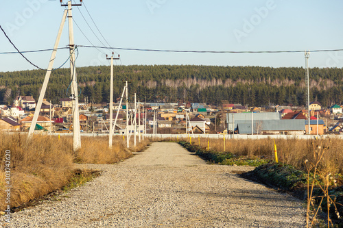 Dirt road with electric poles in a cottage village. Autumn, sunny