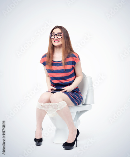 Happy young girl in glasses and a smartphone in her hands sitting on the toilet. Situation concept.