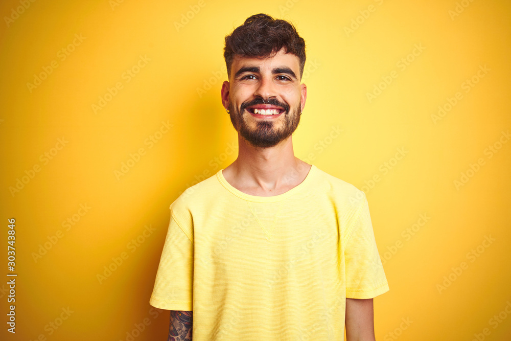 Young man with tattoo wearing t-shirt standing over isolated yellow background with a happy and cool smile on face. Lucky person. Young man with tattoo wearing t-shirt standing over isolated yellow background with a happy and cool smile on face. Lucky person.
