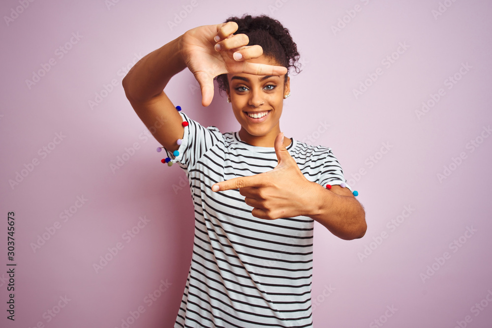 African american woman wearing navy striped t-shirt standing over isolated pink background smiling making frame with hands and fingers with happy face. Creativity and photography concept. African american woman wearing navy striped t-shirt standing over isolated pink background smiling making frame with hands and fingers with happy face. Creativity and photography concept.