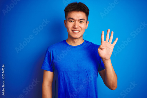 Young asian chinese man wearing t-shirt standing over isolated blue background showing and pointing up with fingers number four while smiling confident and happy. © Krakenimages.com