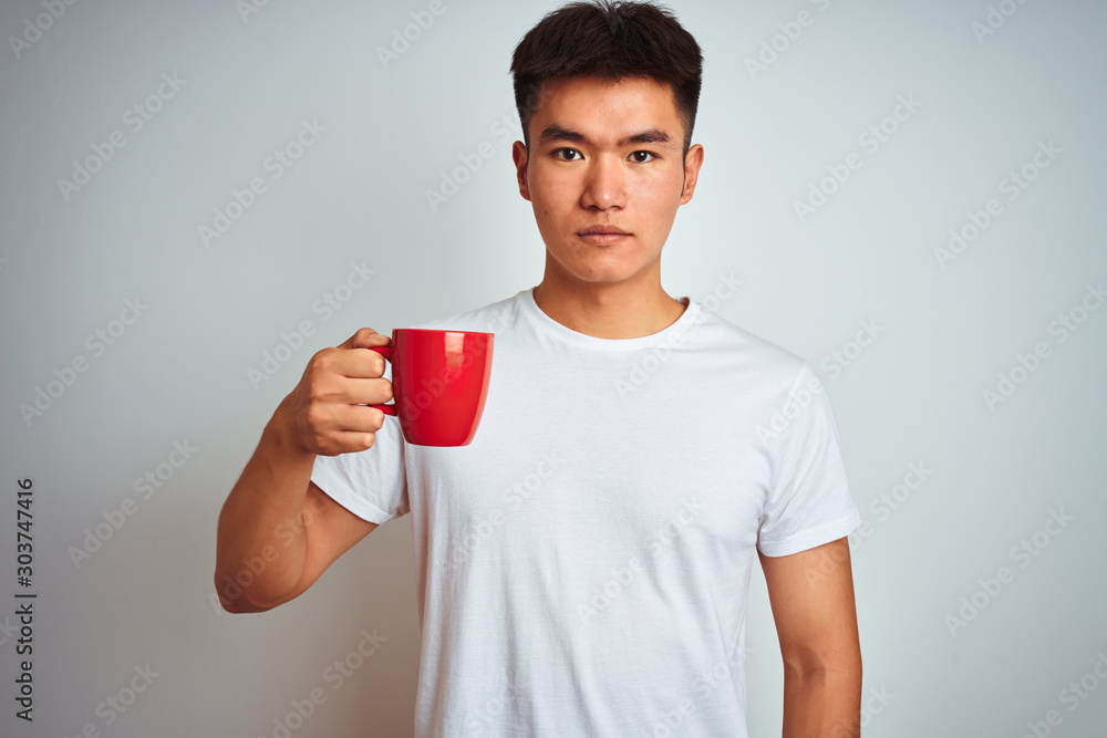 Asian chinese man holding red cup of coffee standing over isolated white background with a confident expression on smart face thinking serious Asian chinese man holding red cup of coffee standing over isolated white background with a confident expression on smart face thinking serious