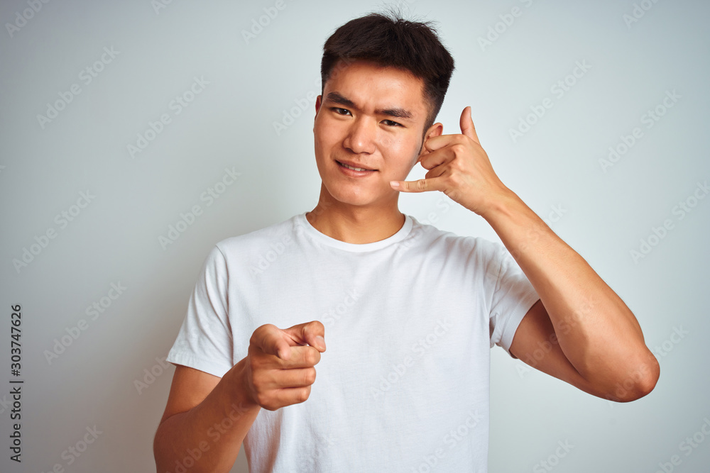 Φωτογραφία Young asian chinese man wearing t-shirt standing over isolated white background smiling doing talking on the telephone gesture and pointing to you