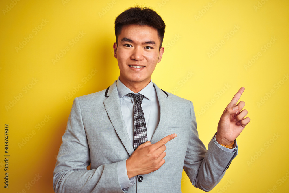 Φωτογραφία Asian chinese businessman wearing suit and tie standing over isolated yellow background smiling and looking at the camera pointing with two hands and fingers to the side