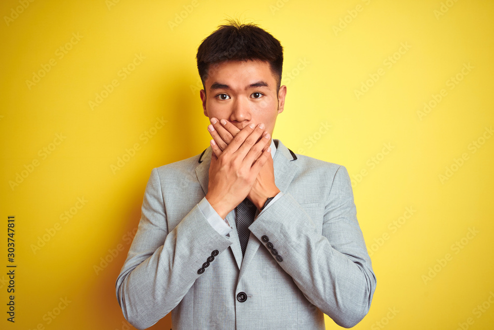 Φωτογραφία Asian chinese businessman wearing suit and tie standing over isolated yellow background shocked covering mouth with hands for mistake