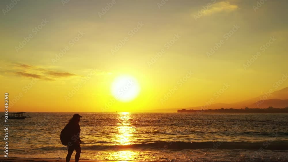 Silhouette of girl with backpack walking along exotic beach at sunset yellow sky reflecting on sea surface in Philippines Silhouette of girl with backpack walking along exotic beach at sunset yellow sky reflecting on sea surface in Philippines