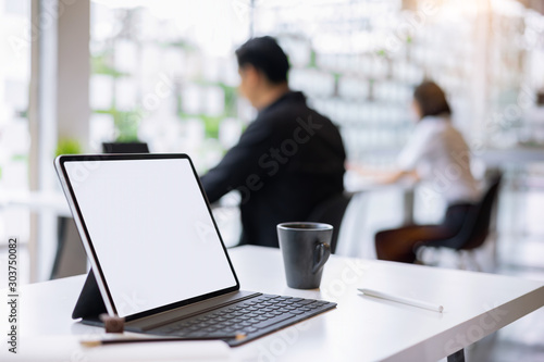 Mockup blank white desktop screen tablet with a man and woman are working in background.