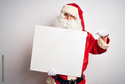 Middle age man wearing Santa Claus costume holding banner over isolated white background very happy pointing with hand and finger © Krakenimages.com