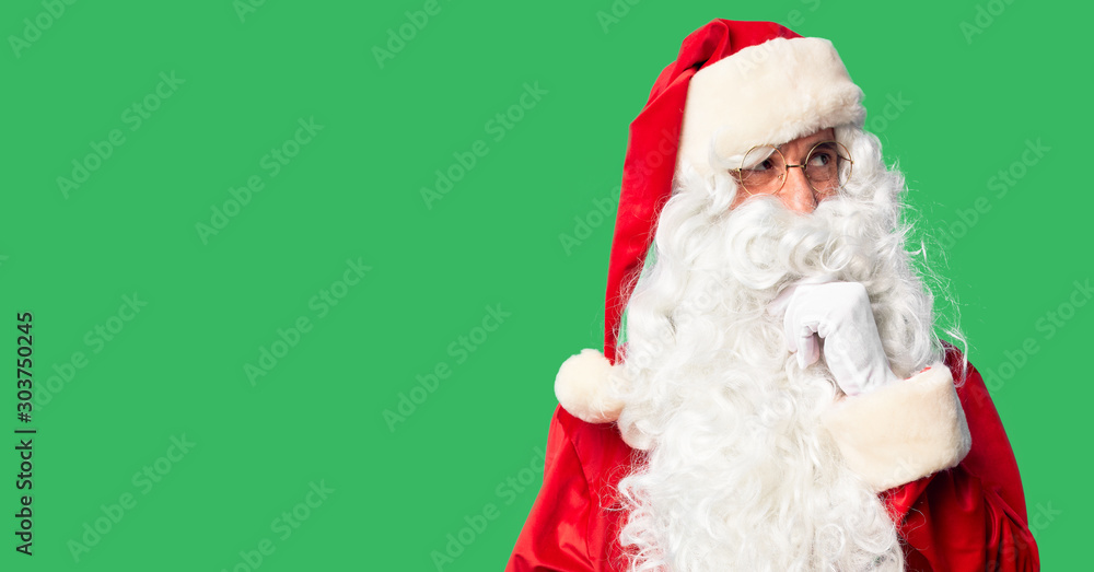 Middle age handsome man wearing Santa Claus costume and beard standing with hand on chin thinking about question, pensive expression. Smiling and thoughtful face. Doubt concept. Middle age handsome man wearing Santa Claus costume and beard standing with hand on chin thinking about question, pensive expression. Smiling and thoughtful face. Doubt concept.