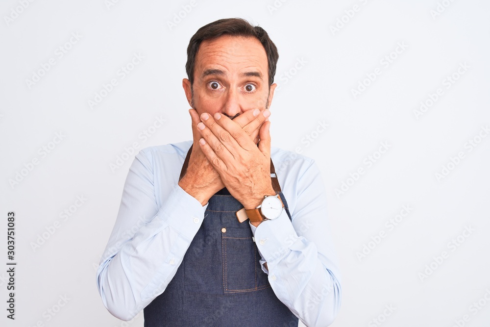 Middle age shopkeeper man wearing apron standing over isolated white background shocked covering mouth with hands for mistake. Secret concept. Middle age shopkeeper man wearing apron standing over isolated white background shocked covering mouth with hands for mistake. Secret concept.