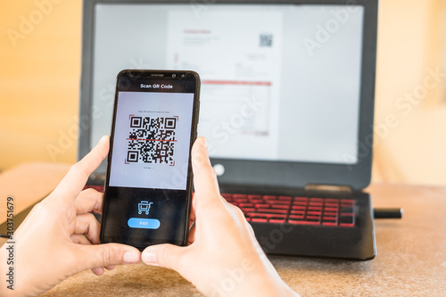 Close up of hand smartphone to make mobile wallet payment via QR code scanning digital invoice from laptop screen. The QR code leads to "Thank you so much" when scanned.