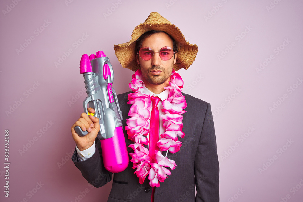 Φωτογραφία Young businessman wearing water gun hawaiian lei hat glasses over isolated pink