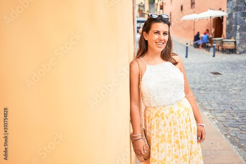 Beautiful girl leaning on orange wall, young friendly woman smiling happy on a sunny day of summer