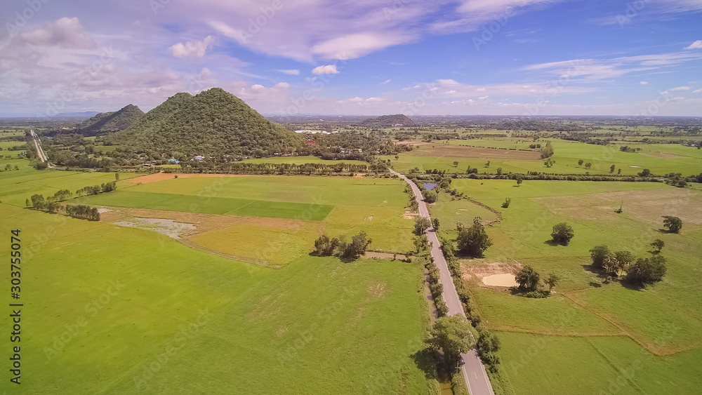 Aerial view above the road, green rice paddy field and village with cloudy sky background, Khao Phra, Tha Muang, Kanchanaburi, West of Thailand.