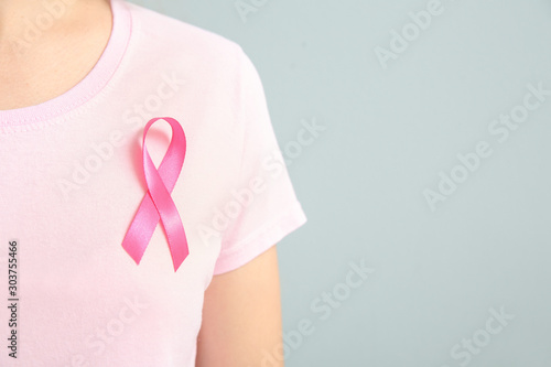 Young woman with pink ribbon on grey background, closeup. Cancer awareness concept