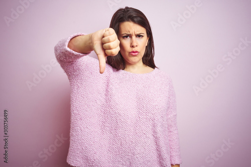 Young beautiful brunette woman wearing a sweater over pink isolated background looking unhappy and angry showing rejection and negative with thumbs down gesture. Bad expression.