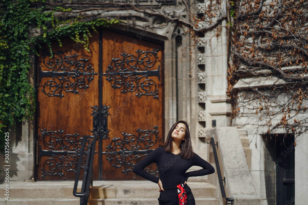 Φωτογραφία stylish brunette standing next to the entance to a building at University of Chi