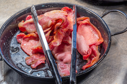Canvas Print Pile of cooked back bacon with tongs