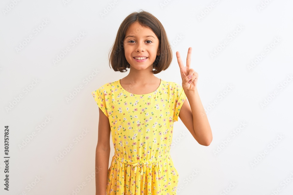 Young beautiful child girl wearing yellow floral dress standing over isolated white background showing and pointing up with fingers number two while smiling confident and happy. Young beautiful child girl wearing yellow floral dress standing over isolated white background showing and pointing up with fingers number two while smiling confident and happy.