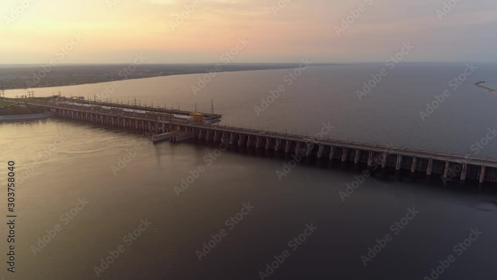 Helicopter largest hydropower plant hydroelectric power station is a cement dam reservoir on a wide deep-water river. Cars go traffic. Water supply irrigation. Sunset city industrial landscape Helicopter largest hydropower plant hydroelectric power station is a cement dam reservoir on a wide deep-water river. Cars go traffic. Water supply irrigation. Sunset city industrial landscape