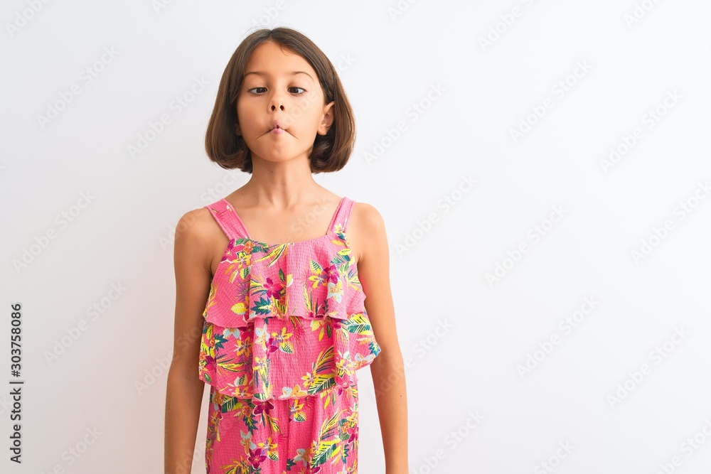 Young beautiful child girl wearing pink floral dress standing over isolated white background making fish face with lips, crazy and comical gesture. Funny expression. Young beautiful child girl wearing pink floral dress standing over isolated white background making fish face with lips, crazy and comical gesture. Funny expression.