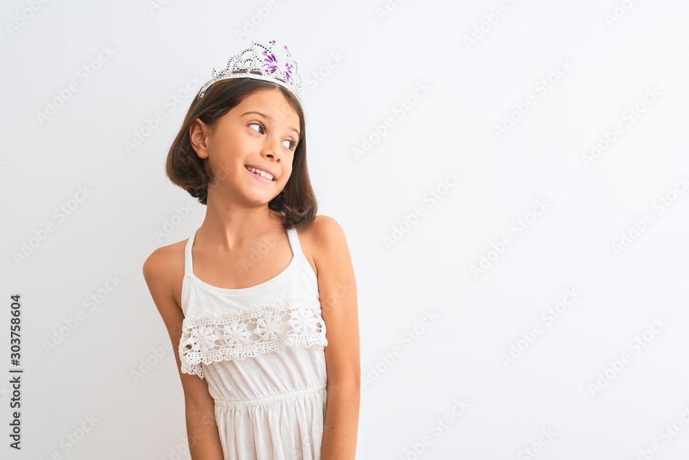 Beautiful child girl wearing princess crown standing over isolated white background looking away to side with smile on face, natural expression. Laughing confident. Beautiful child girl wearing princess crown standing over isolated white background looking away to side with smile on face, natural expression. Laughing confident.