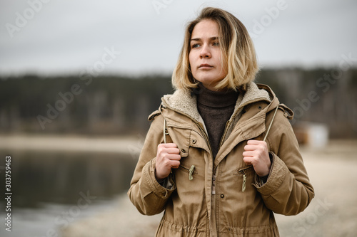 a young girl in a warm winter jacket is walking with a backpack along the seashore and with a serious look looks away