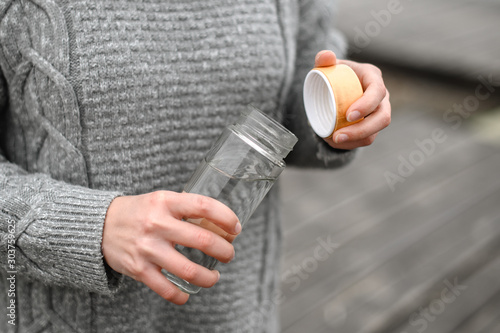 close-up of female hands in a woolen sweater opening a refillable glass water bottle