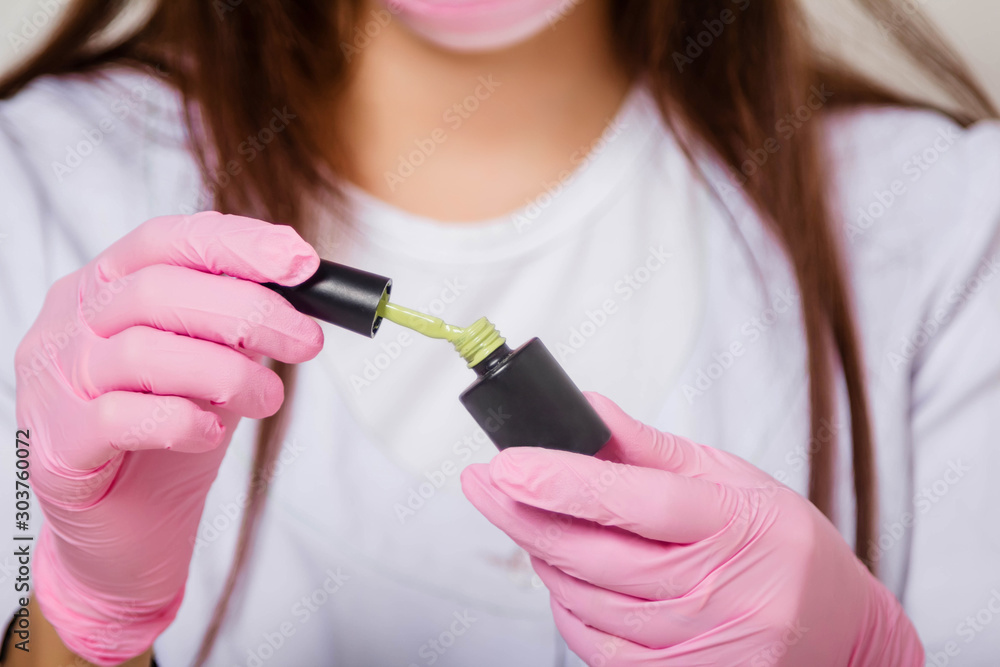 Φωτογραφία A girl in a white coat, mask and gloves holds in her hands a bottle with varnish and a brush