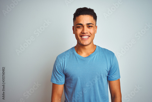 Young brazilian man wearing blue t-shirt standing over isolated white background with a happy and cool smile on face. Lucky person.