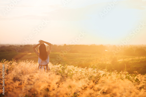 Trendy girl in stylish summer dress feeling free in the field with flowers in sunshine. © max_play
