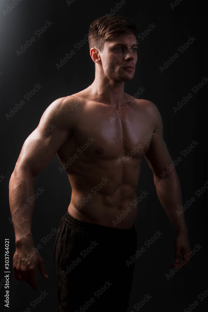 Muscular bodybuilder posing with a naked torso on a black background in the dark with backlight. Sexy man.