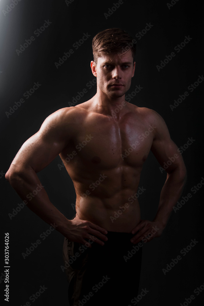 Muscular bodybuilder posing with a naked torso on a black background in the dark with backlight. Sexy man. Muscular bodybuilder posing with a naked torso on a black background in the dark with backlight. Sexy man.