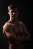 Muscular bodybuilder posing with a naked torso on a black background in the dark with backlight. Sexy man.