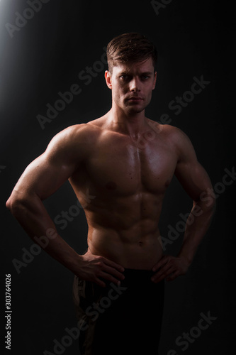 Muscular bodybuilder posing with a naked torso on a black background in the dark with backlight. Sexy man. © Михаил Гута