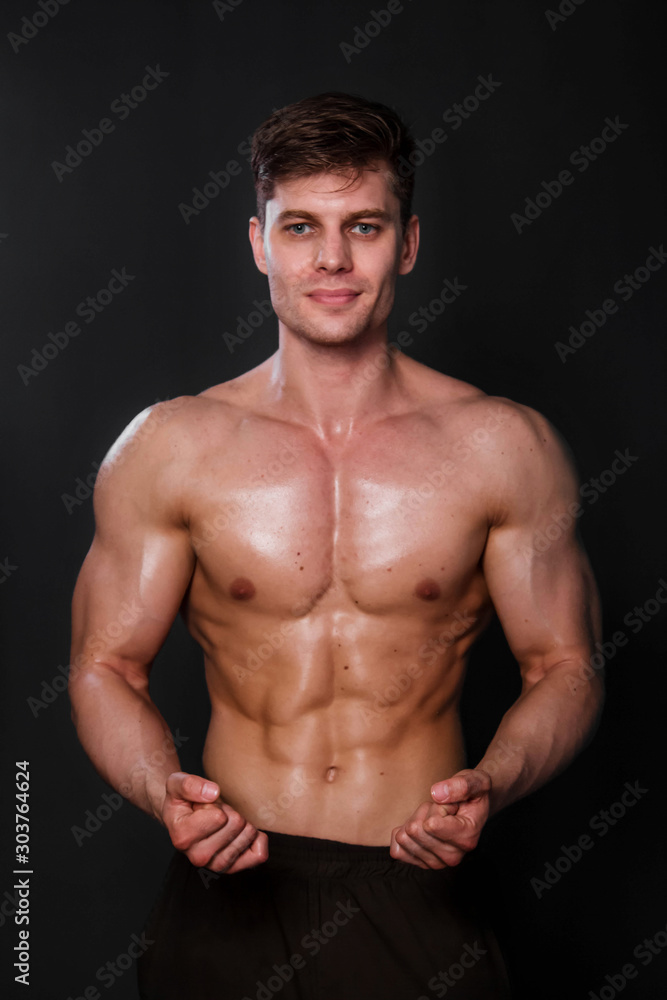 Muscular bodybuilder posing with a naked torso against a black background. Sexy man.