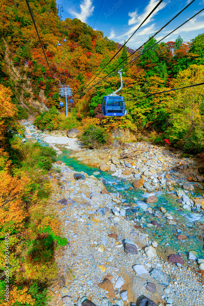 Φωτογραφία The Naeba-Tashiro Dragondola, Japans longest ropeway passes over a crystal clear mountain river with trees bearing Autumnal fall colored leaves at Naeba, Yuzawa, Niigata, Japan