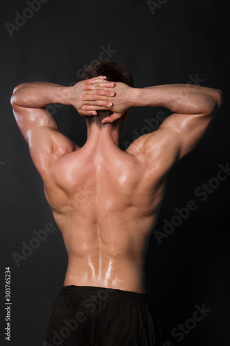 Muscular bodybuilder man posing on black background. View from the back.