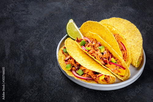 Cochinita pibil taco shells, a Mexican snack with pulled pork, avocado and marinated red onion, a close-up shot on a dark background with a place for text