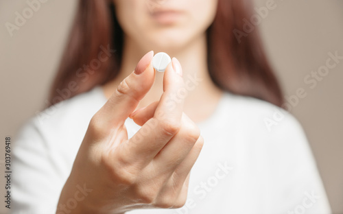 Woman holding a white round pill or vitamin.